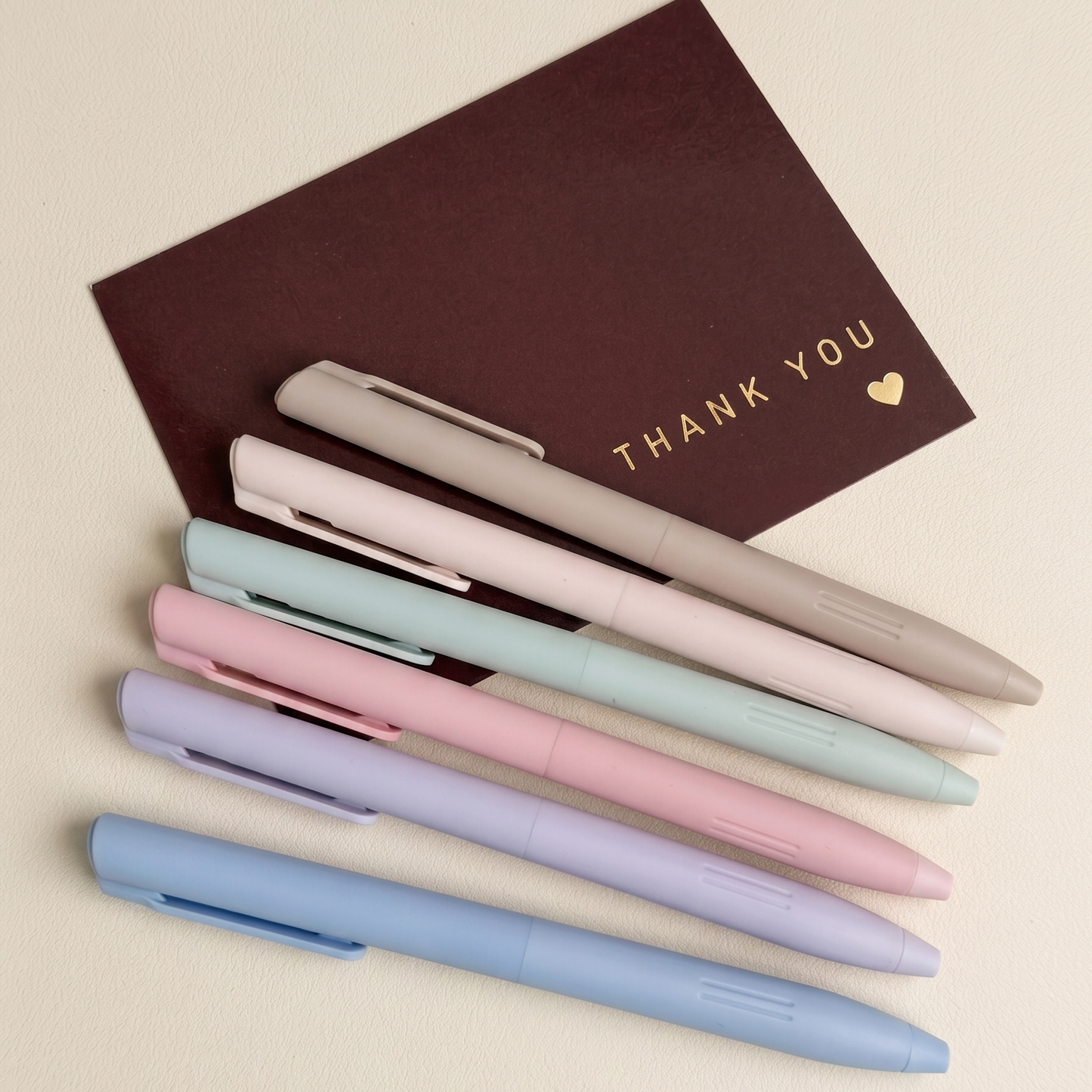 Set of pastel-colored pens and a brown notebook on a beige background