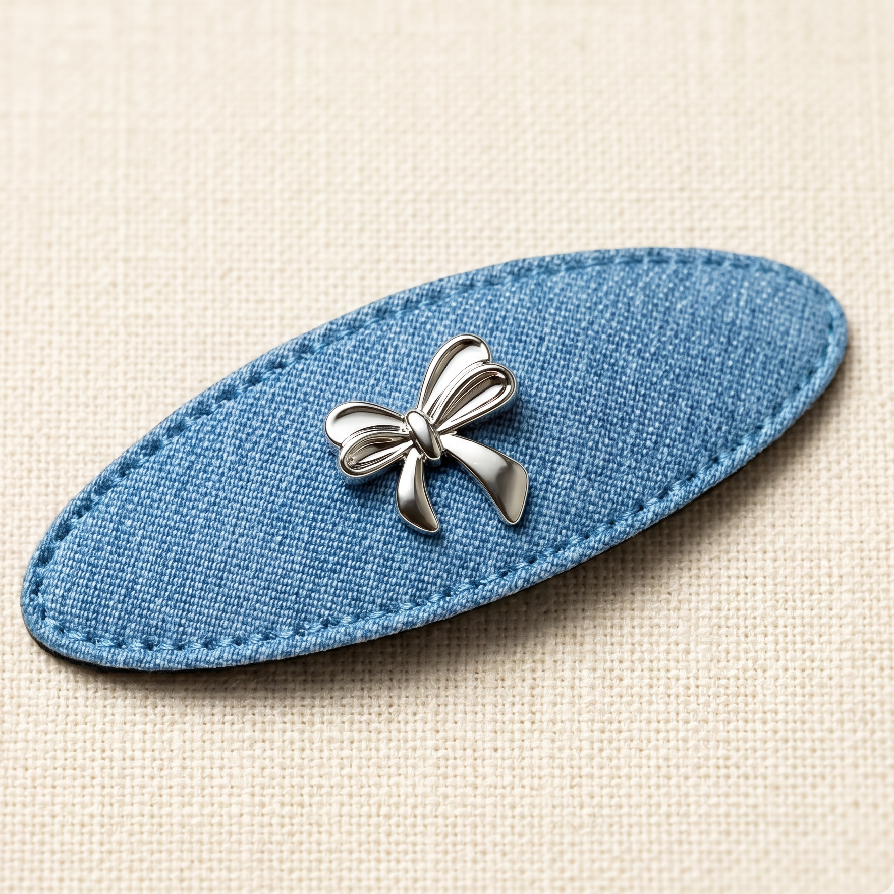 Blue oval fabric hair clip with a silver bow design on a beige background