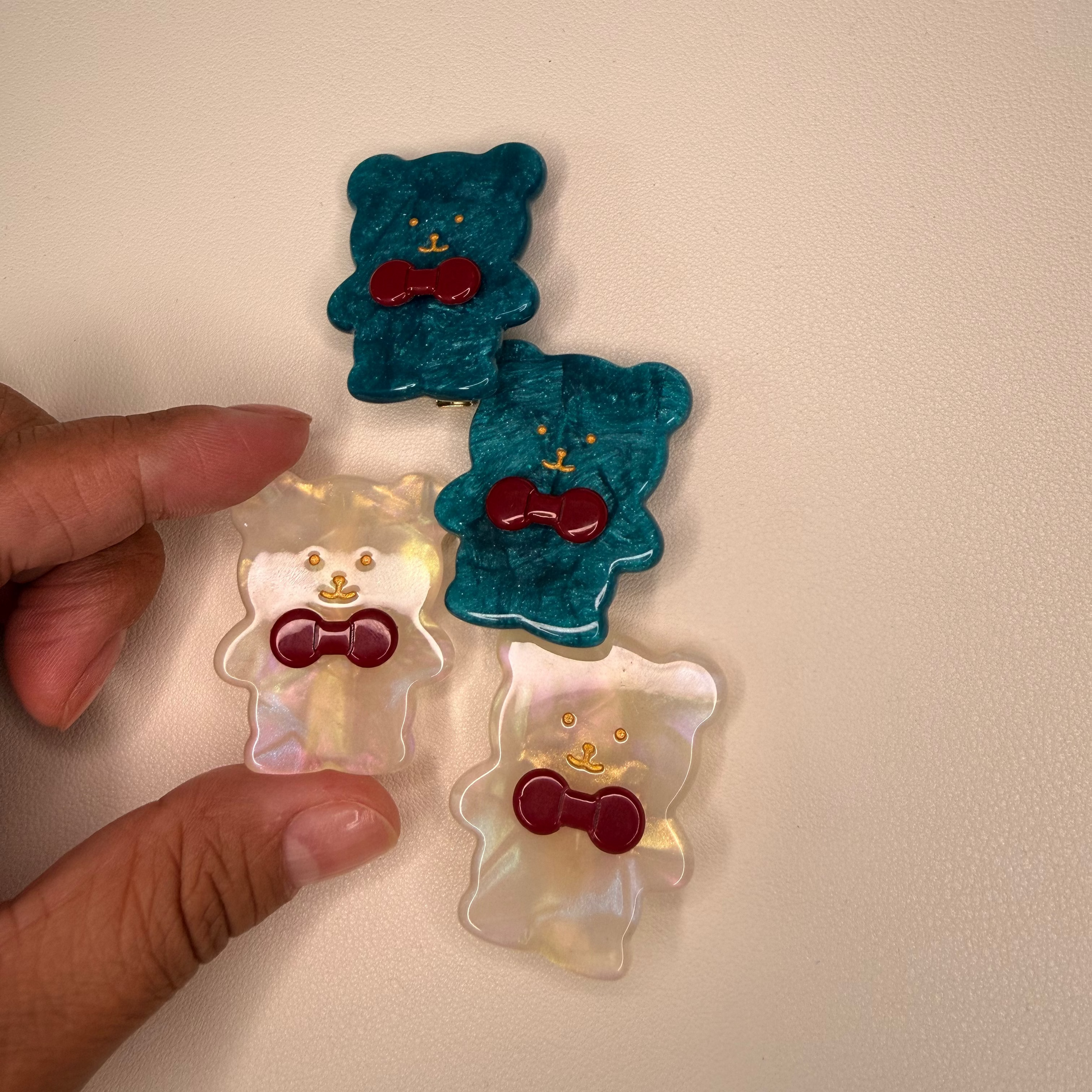 Hand holding bear-shaped cookies with red bow ties on a beige background